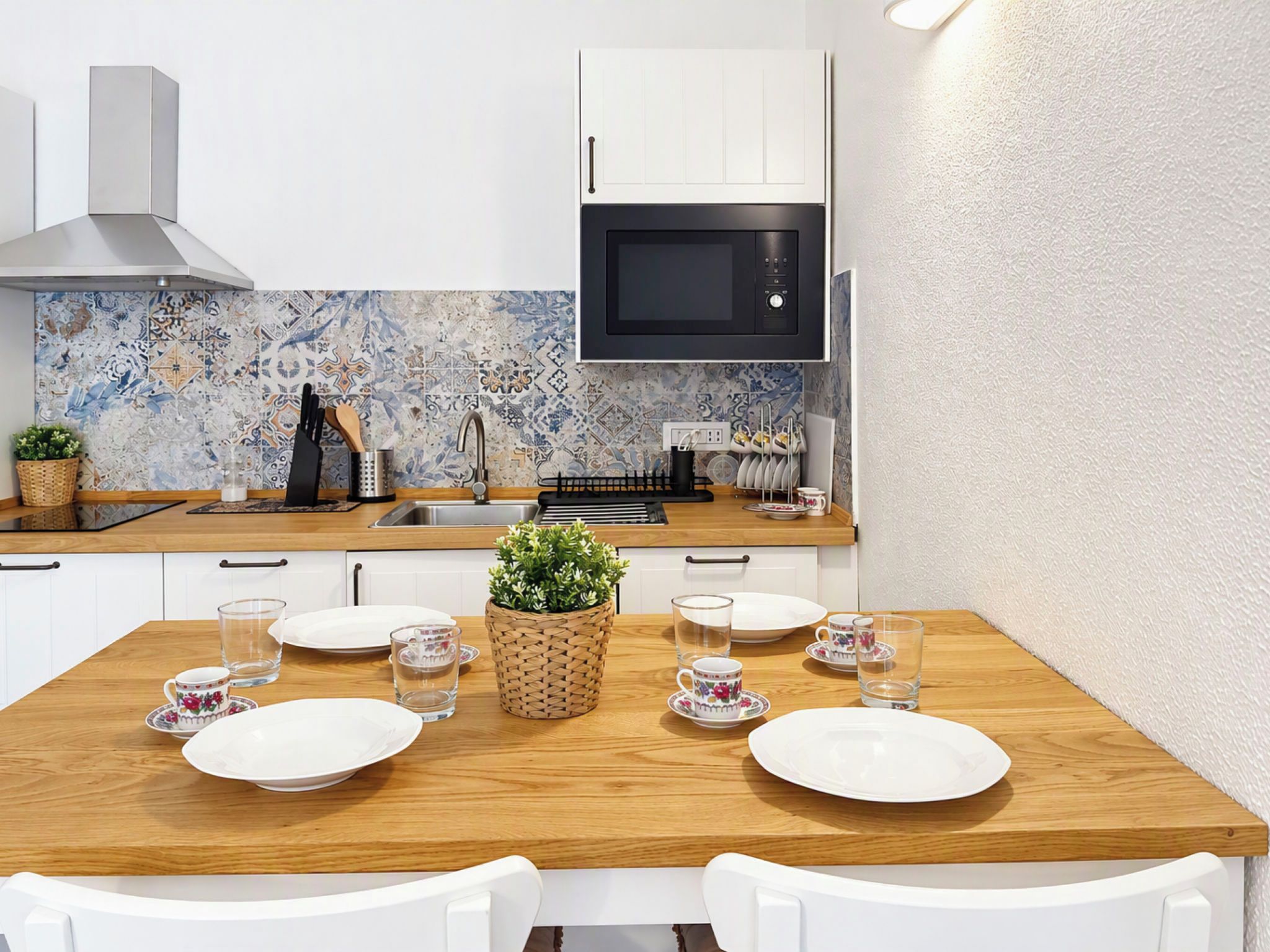 Une cuisine moderne avec des meubles blancs, un micro-ondes noir et un pare-feu en carreaux.