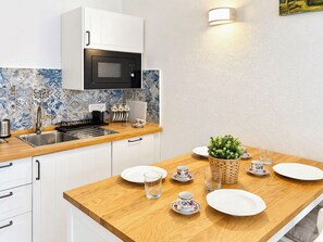Une cuisine moderne avec des meubles blancs, un four à micro-ondes et un évier. On y trouve un plan de travail en bois agrémenté d'une plante et d'un service à thé.