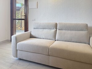 A beige sofa in a room with a textured wall and a window. - Porto Luna 1 by Interhome (Villasimius)