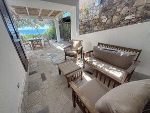 A patio with a stone floor, wooden furniture, and a view of the sea. - Porto Luna 1 by Interhome (Villasimius)
