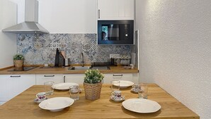 Une cuisine moderne avec des armoires blanches, une hotte en acier inoxydable, un dosseret carrelé et une table à manger en bois, mise avec des assiettes et des verres.