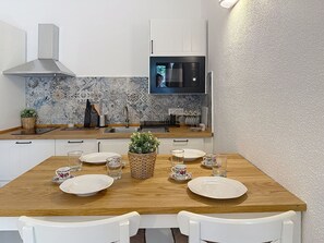 A modern kitchen with white cabinets, a stainless steel range hood, a tiled backsplash, and a wooden dining table set with plates and glasses. - Porto Luna 1 by Interhome (Villasimius)