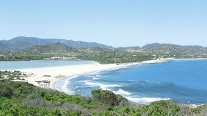 Un paysage côtier avec une plage, un ciel dégagé et des montagnes à l’horizon.