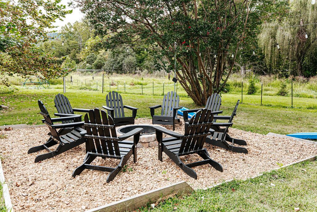 Un patio con sillas Adirondack dispuestas alrededor de una mesa, rodeado por una zona de grava y una cerca.