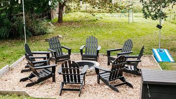 Un’area salotto circolare con poltrone Adirondack attorno a un braciere, circondata da ghiaia ed erba.