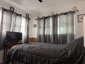 A bedroom with a bed, a TV, a chair, and curtains.