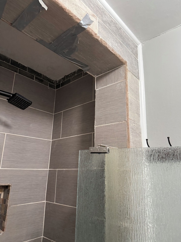 Une salle de bain avec des murs carrelés, une pomme de douche et un plafond partiellement achevé.