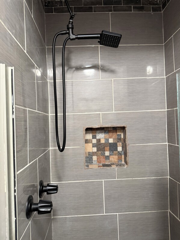 A shower area with a handheld showerhead, a wall-mounted control, and a small decorative tile feature.
