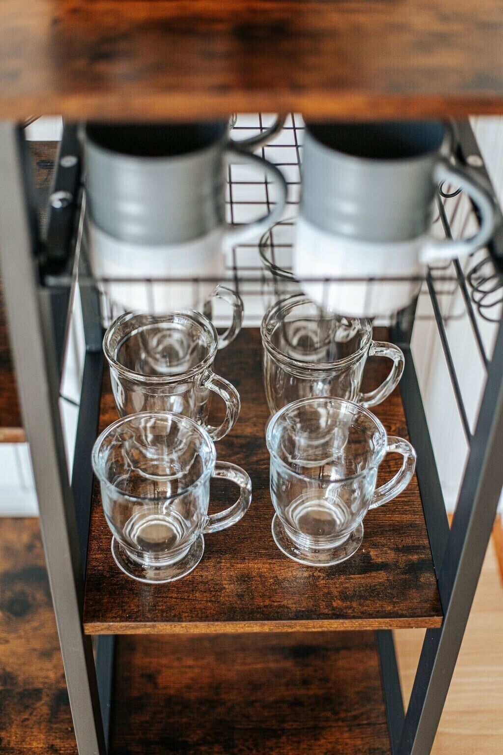 A kitchen area with a coffee maker and four clear glass cups on a rack.