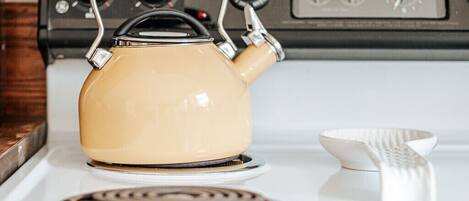 A kitchen with a stove, a kettle, and a white bowl.