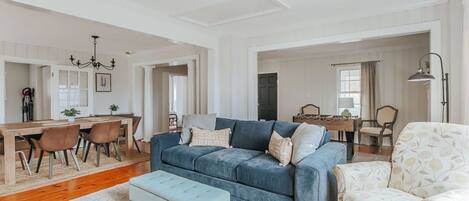 Un salon spacieux avec un canapé bleu, un coin repas avec une table et des chaises en bois, et un fauteuil à motifs.