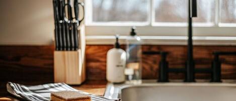 A kitchen counter with a knife block, a bottle of dish soap, and a slice of cake on a plate.