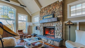 A cozy living room with a stone fireplace, leather furniture, and large windows. - Art & Soul Main House (Nellysford)