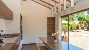 A modern kitchen with a built-in oven, a dining area with a bench, and a view of an outdoor patio with umbrellas. - Villa with top-of-the-range amenities Swimming pool and fitness room (San-Gavino-di-Carbini)