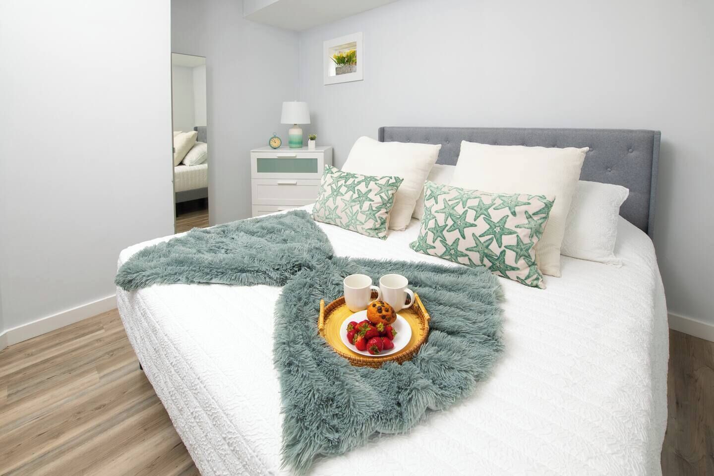 A neatly made bed with a fluffy blanket, pillows with a star pattern, and a tray with strawberries and coffee cups.