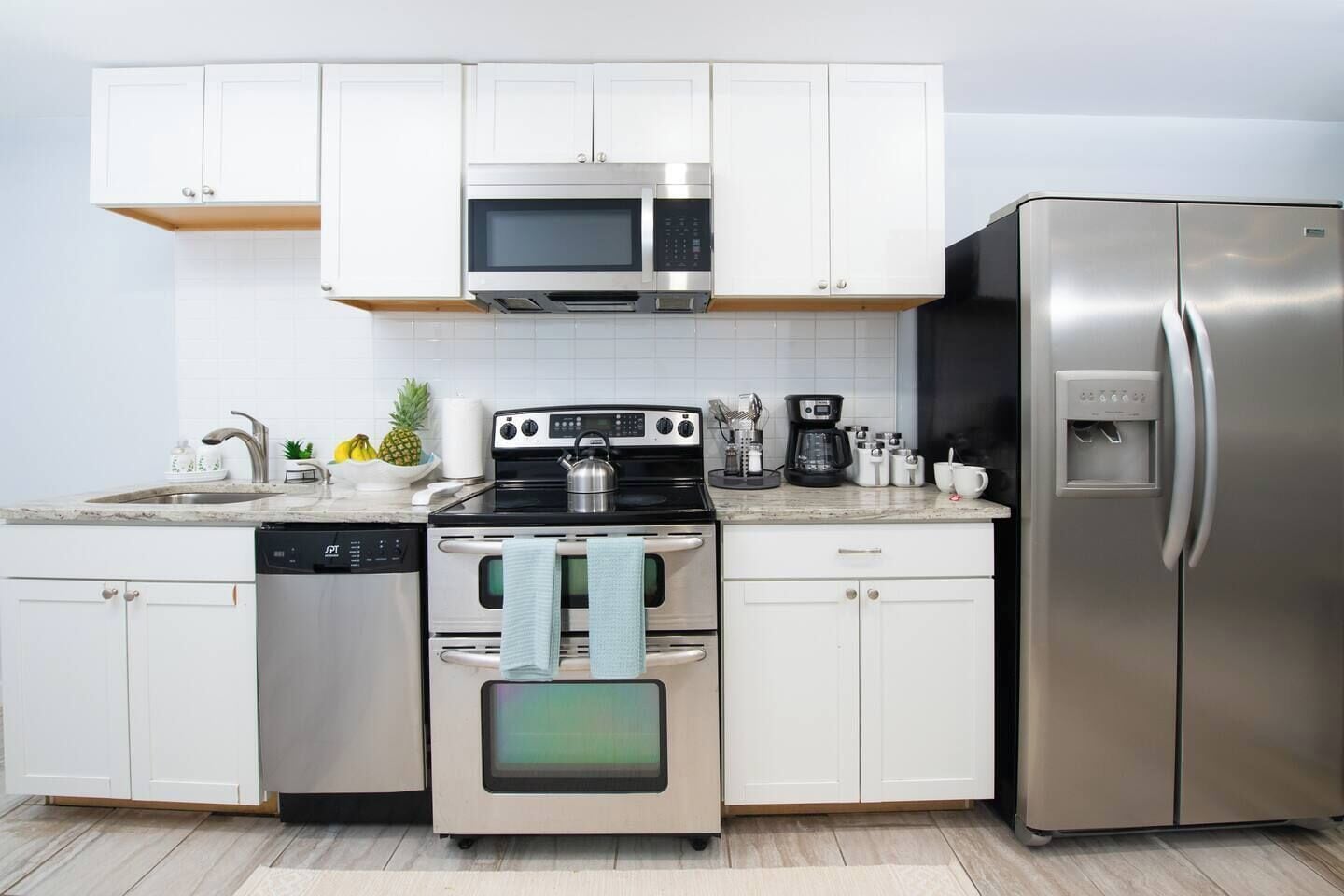 A modern kitchen with white cabinets, stainless steel appliances, and a built-in dishwasher.