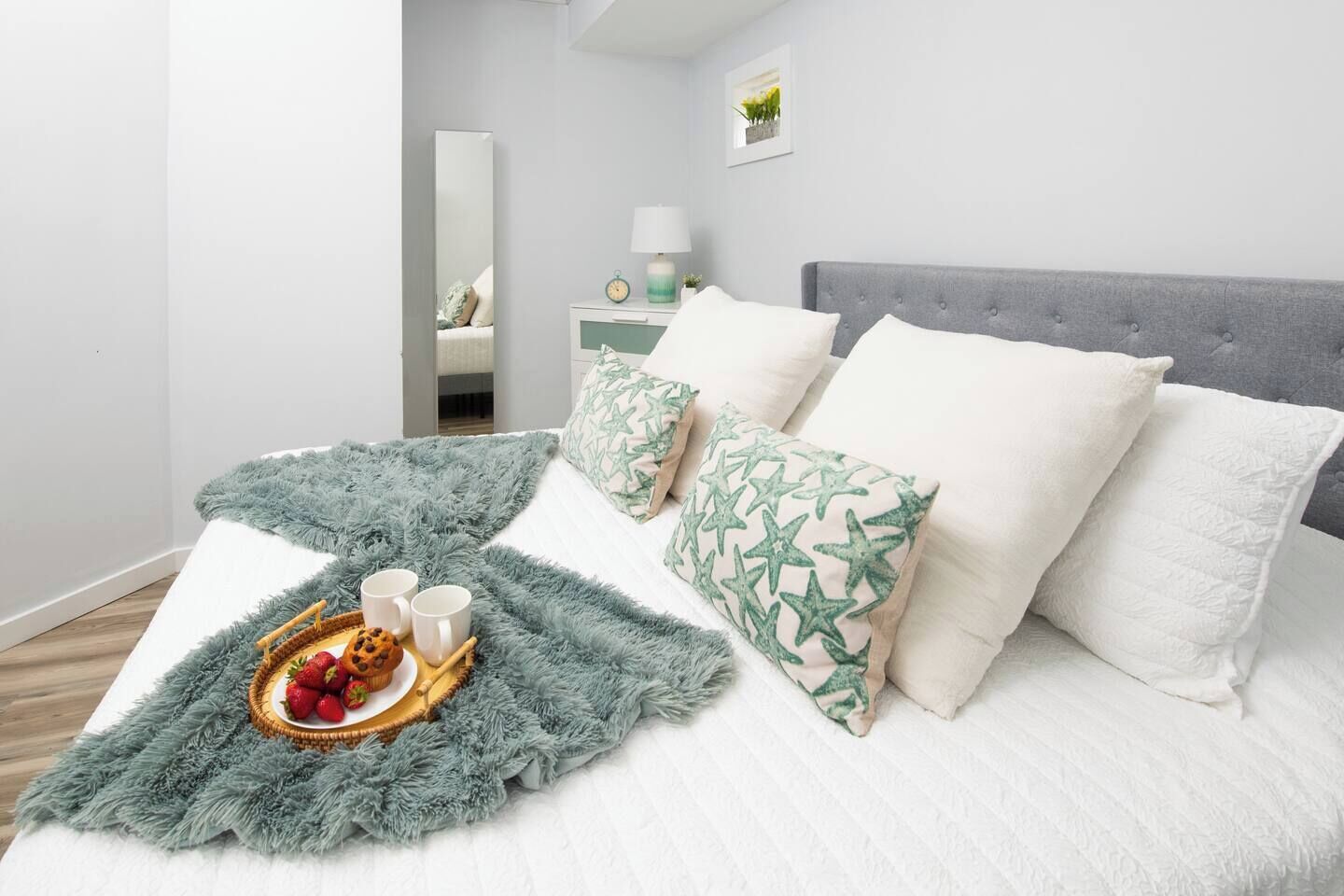 A neatly made bed with a fluffy blanket, pillows with a leaf pattern, and a tray with strawberries and two mugs.