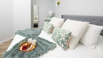 A neatly made bed with a fluffy blanket, pillows with a leaf pattern, and a tray with strawberries and two mugs.