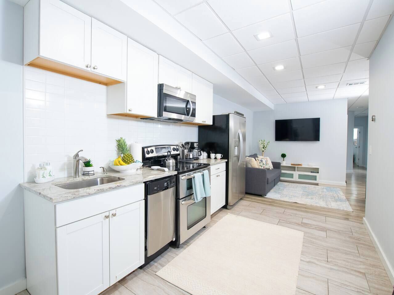 A modern kitchen with white cabinets, stainless steel appliances, and a flat-screen TV mounted on the wall.