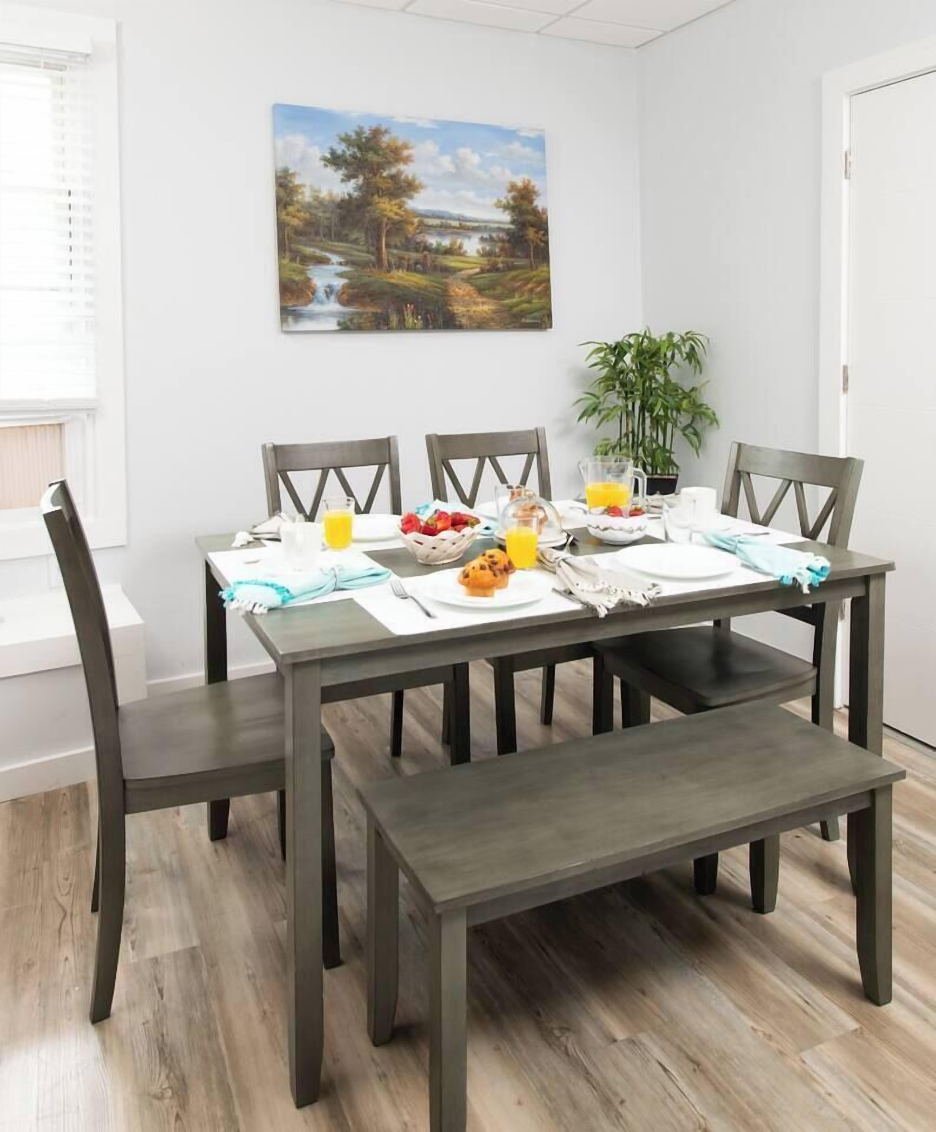 A dining table with chairs, a bench, and a breakfast setting including a bowl of fruit, a jug of orange juice, and a cup.