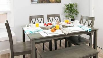 A dining table with chairs, a bench, and a breakfast setting including a bowl of fruit, a jug of orange juice, and a cup.