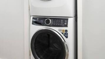 A stacked washer and dryer unit in a corner of a room with wooden flooring.