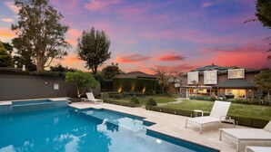 Ein Swimmingpool mit Liegestühlen, ein gepflegter Rasen und ein Haus mit modernem Design.