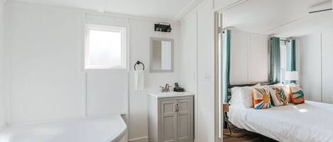 A bedroom with a bed, a nightstand, a dresser, a window, and a bathroom with a toilet and sink.