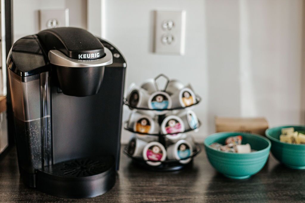 Una cafetera Keurig sobre una encimera de cocina, con un portaluces para tazas y dos cuencos verde azulado.