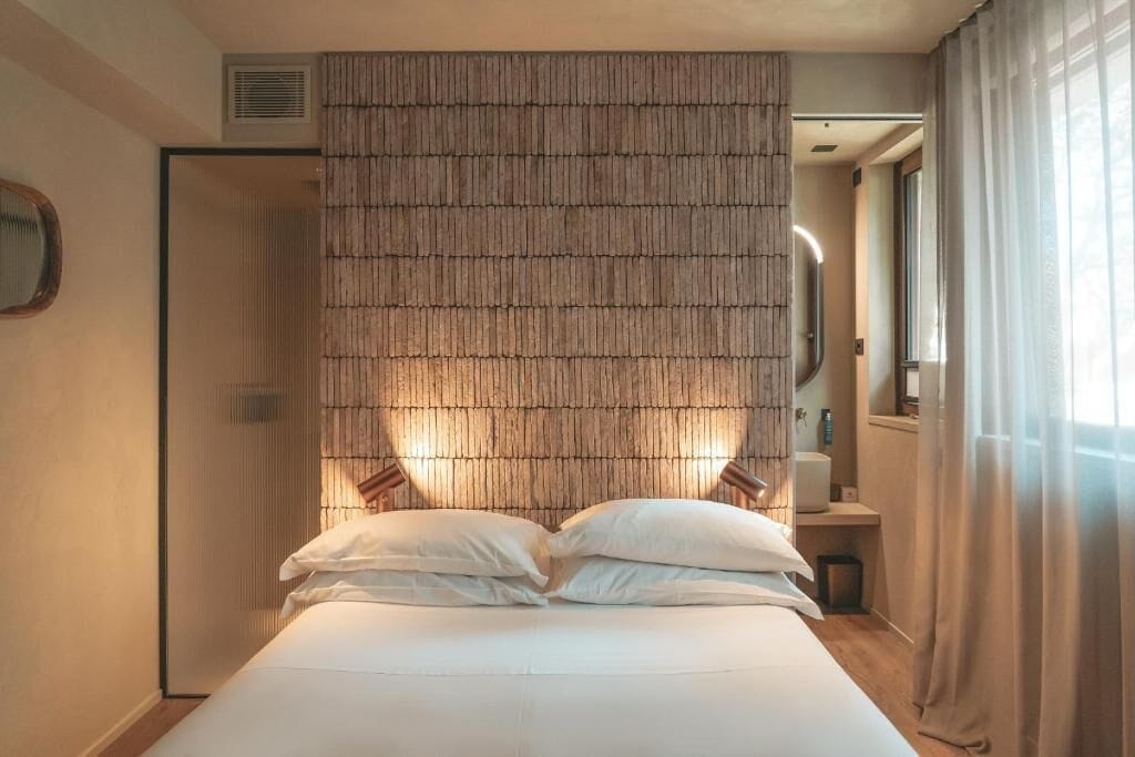 A bedroom with a bed, a wall with vertical slats, a window with curtains, and a door.