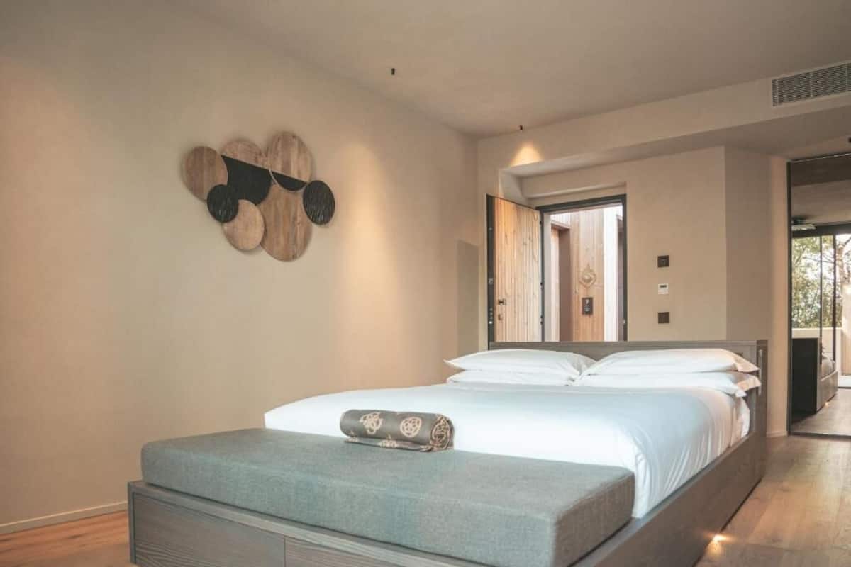 A modern bedroom with a bed, a bench, and a wall-mounted decorative piece.