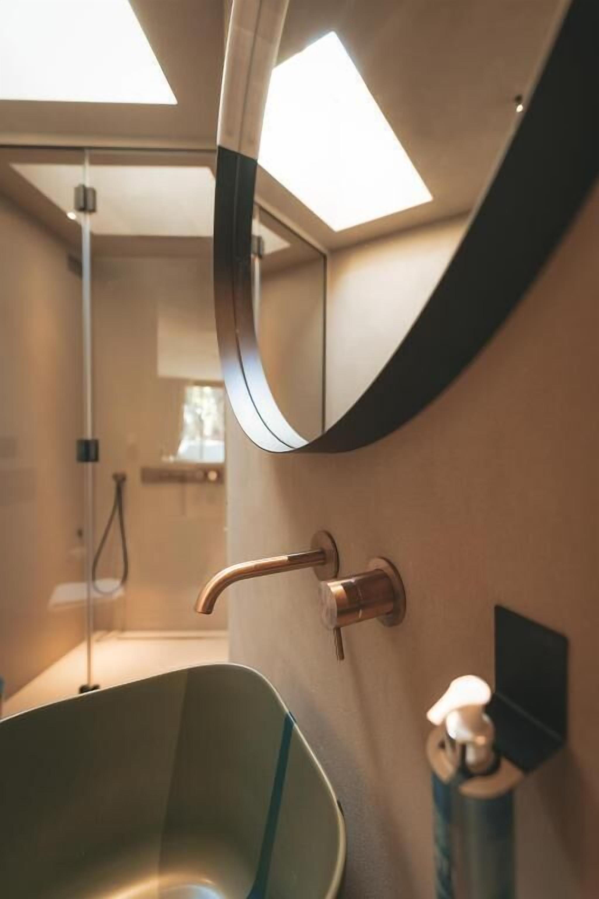 Un baño con un lavabo de vidrio, un espejo curvo y una zona de ducha.