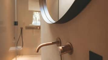 Un baño con un lavabo de vidrio, un espejo curvo y una zona de ducha.
