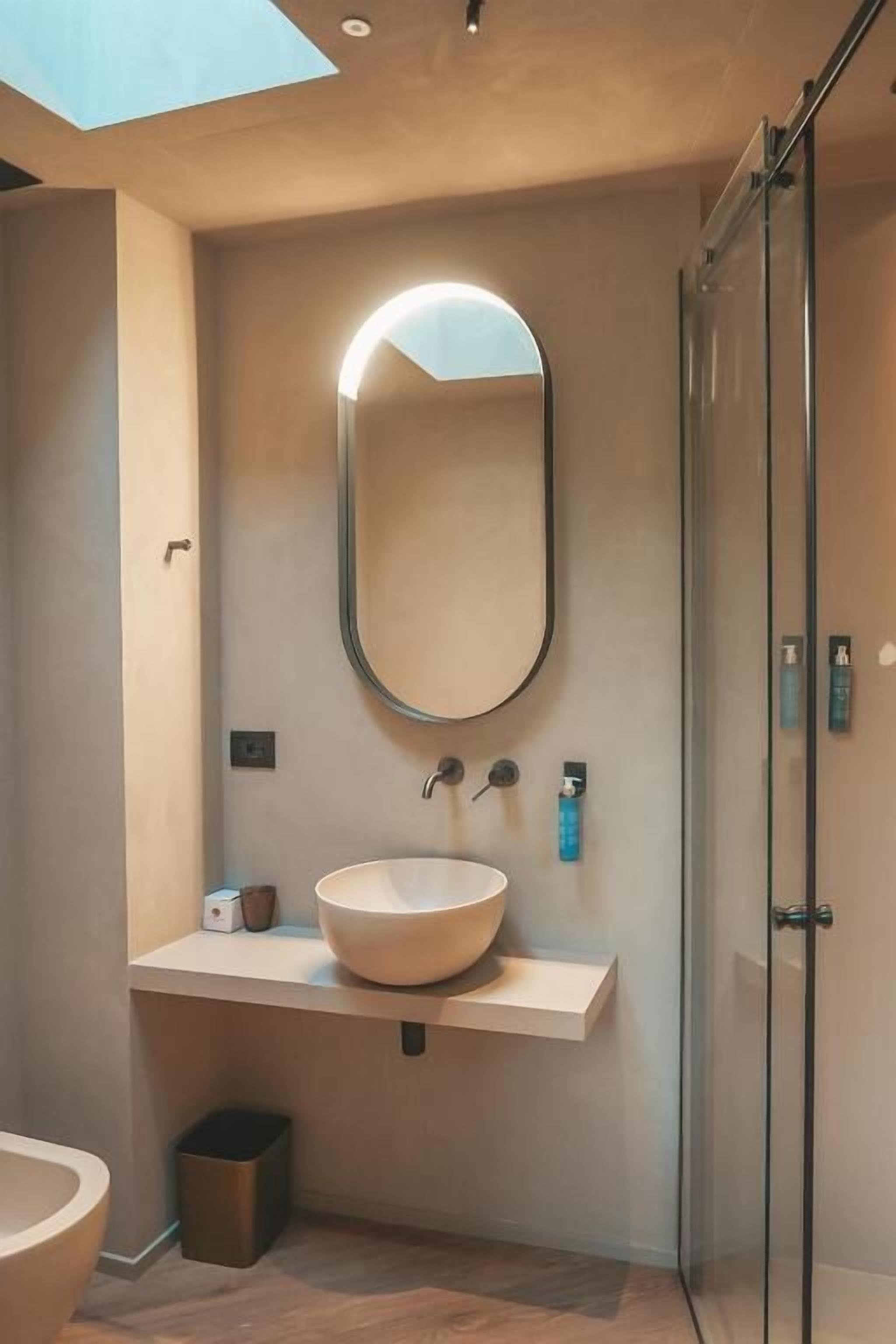 Un bagno moderno con un ampio specchio ovale, un lavabo a incasso e una cabina doccia in vetro.