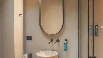 Un bagno moderno con un ampio specchio ovale, un lavabo a incasso e una cabina doccia in vetro.