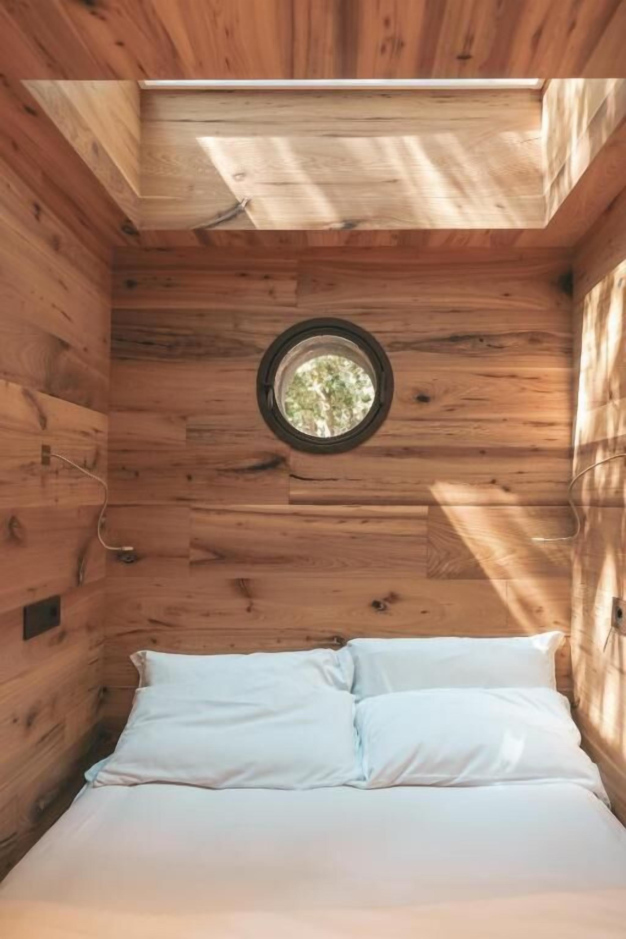 L’intérieur d’un chalet en bois, avec un lit, une lucarne circulaire et des murs en bois.