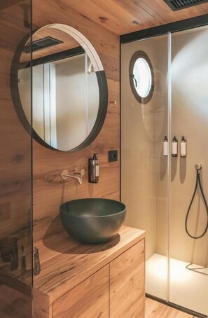 Une salle de bain moderne avec un meuble-lavabo en bois, un miroir rond, un grand lavabo sur pied et une douche à l’italienne.