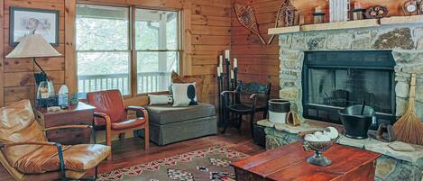 A cozy cabin interior with a stone fireplace, leather furniture, and a large window.