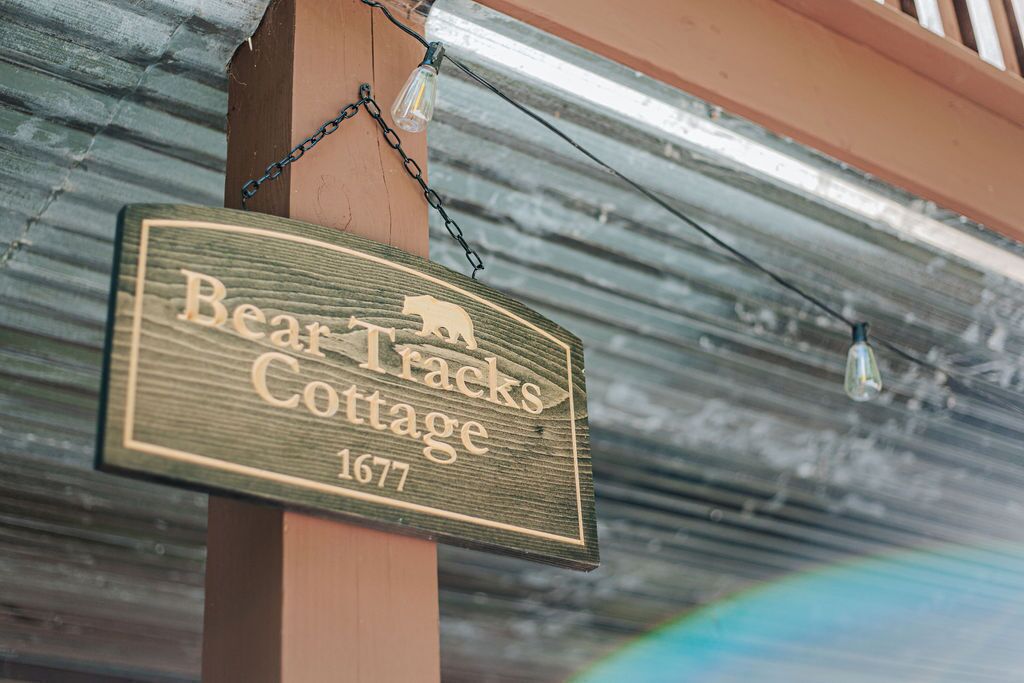 Une pancarte en bois portant l’inscription « Bear Tracks Cottage 1677 » est suspendue à un poteau en bois.