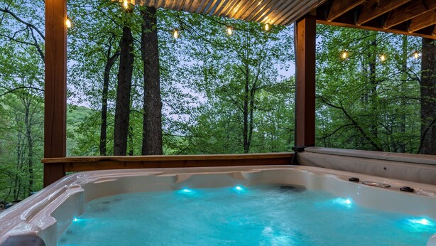 Een hottub met een houten terras en uitzicht op een bos.