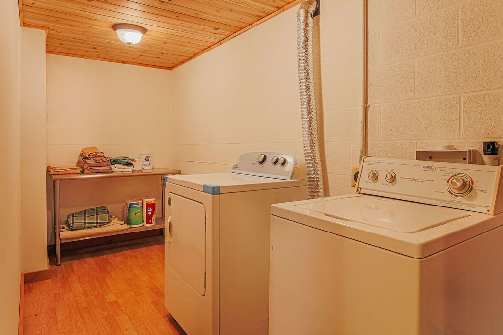 A laundry room with two washing machines, a drying machine, a shelf with folded clothes, and a shower curtain.