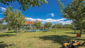 Ein Wohnhaus mit Swimmingpool, Laube und Rasen mit Rasenmäher.