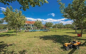 Ein Wohnhaus mit Swimmingpool, Laube und Rasen mit Rasenmäher.