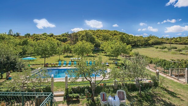 Ein Poolbereich mit Liegestühlen und Sonnenschirmen, umgeben von viel Grün und Hügeln.
