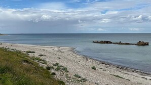 Un paisaje costero con una playa de guijarros, mar tranquilo y cielo nublado.