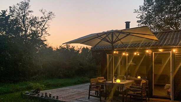 Una terraza de madera con mobiliario exterior y un paraguas grande.