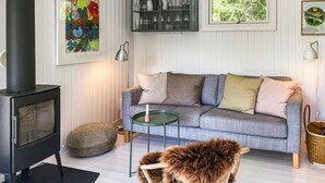 Una sala de estar con un sofá, una mesita, un sillón decorativo, una chimenea y obras de arte en las paredes.