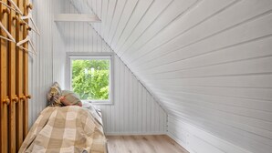 Un dormitorio con ventana, listones de madera en el techo y una cama con manta a cuadros.