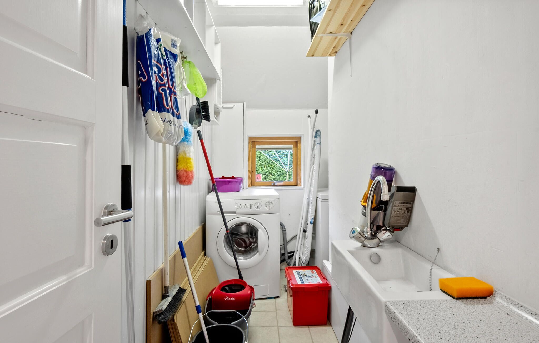 A compact laundry room with a washing machine, a mopping bucket, and a vacuum cleaner.