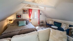 A cozy attic bedroom with a bed, a sofa, a small table, and a chandelier. - 1 bedroom gorgeous apartment in Gudhjem (Gudhjem)